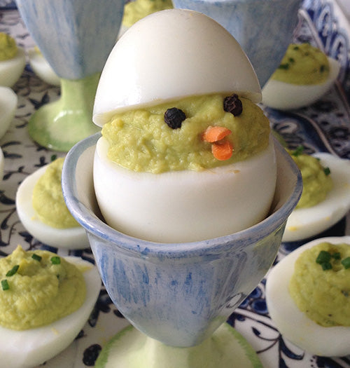 Creative spicy avocado deviled eggs decorated as baby chicks, featuring creamy avocado-honey filling with habanero kick, served in a vintage blue egg cup.