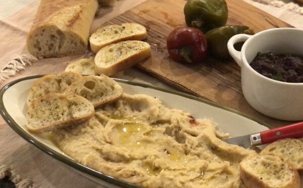 Homemade Tuscan white bean spread drizzled with premium rosemary-infused olive oil, served with crusty artisanal bread slices