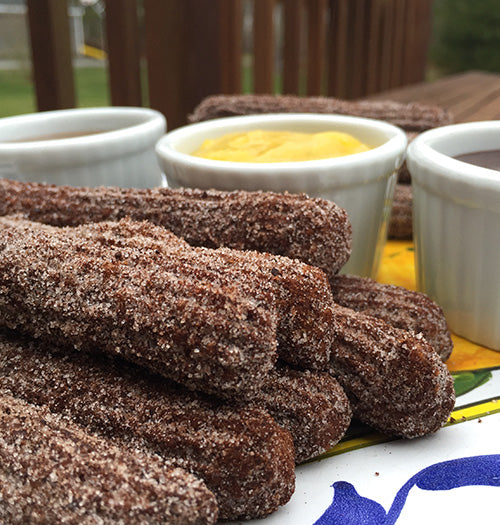 Freshly fried Blood Orange Espresso Churros alongside gourmet dipping sauces, showcasing our Gustare Blood Orange Extra Virgin Olive Oil which creates a uniquely flavorful dessert.