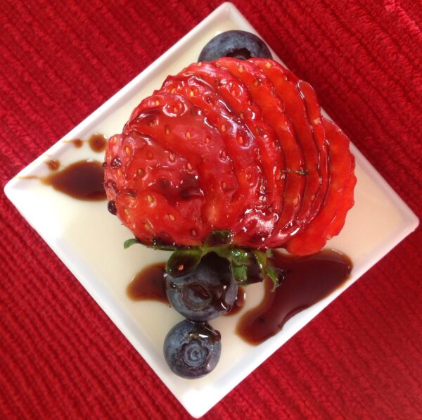 Buttermilk Panna Cotta drizzled with our signature Organic Balsamic Glaze, garnished with fresh strawberries and blueberries, showcasing our gourmet vinegar's versatility in elegant desserts.