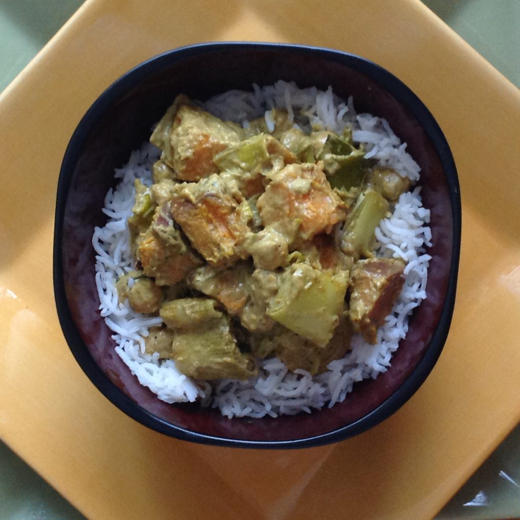 Creamy vegan sweet potato leek and chickpea coconut curry made with Gustare Garlic Extra Virgin Olive Oil, served over basmati rice in a dark bowl