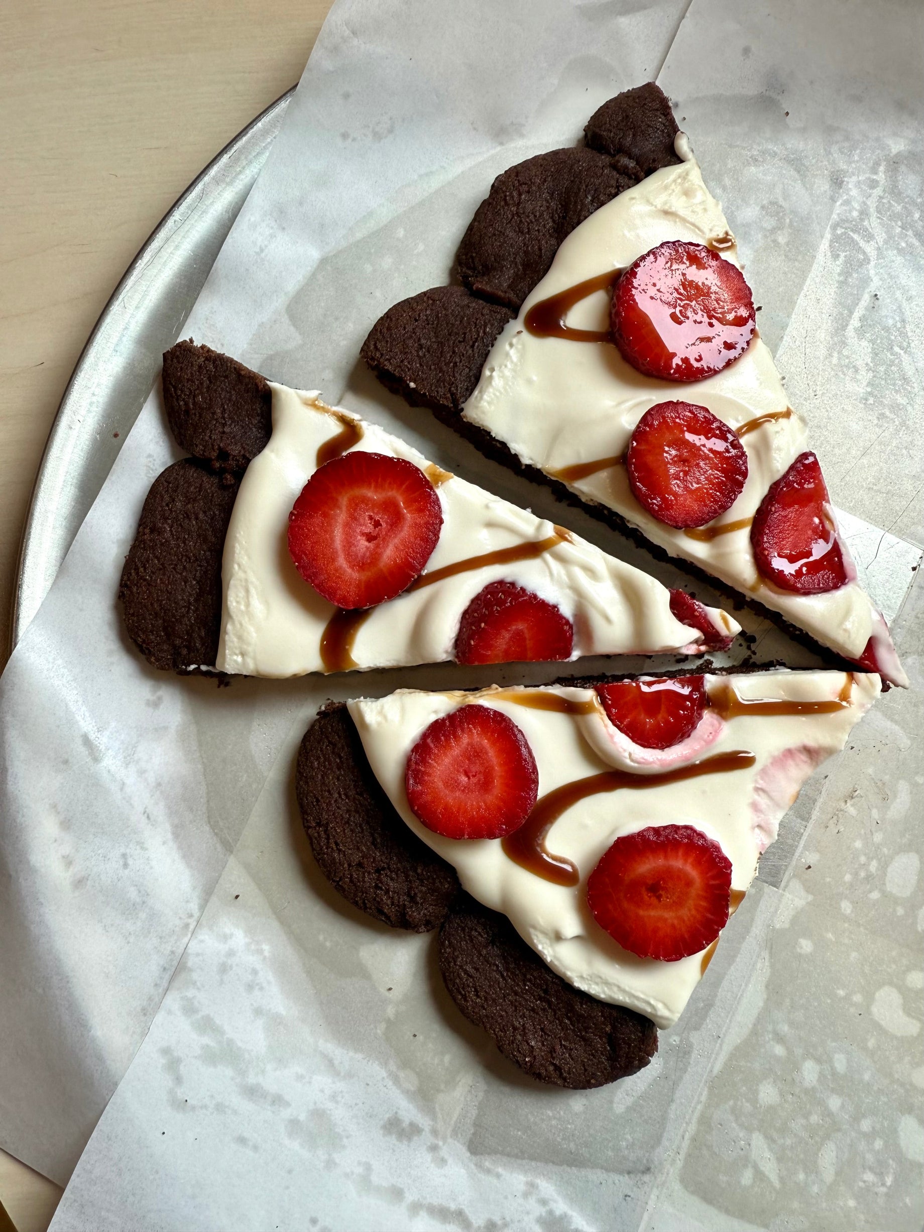 Sliced chocolate cookie pizza with white mascarpone sauce, fresh strawberry slices, and balsamic drizzle