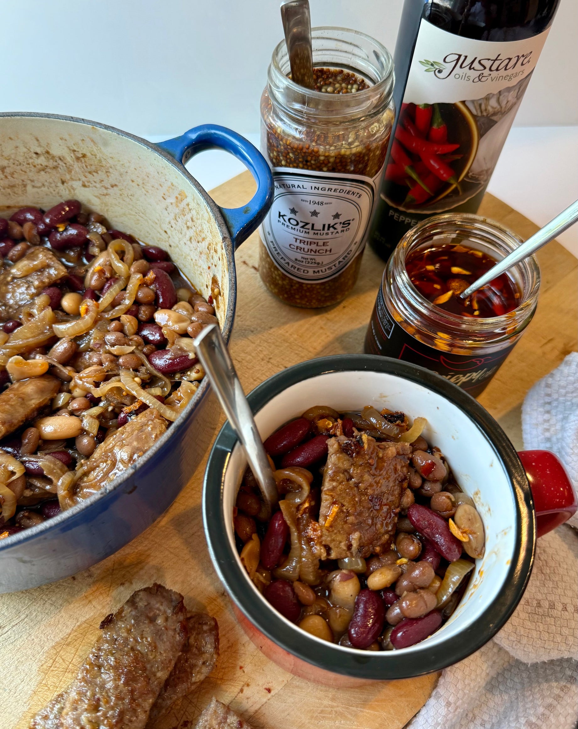 Gourmet baked beans and sausage recipe showcasing Gustare's premium espresso balsamic vinegar, maple balsamic, and pepperoncino garlic olive oil products.