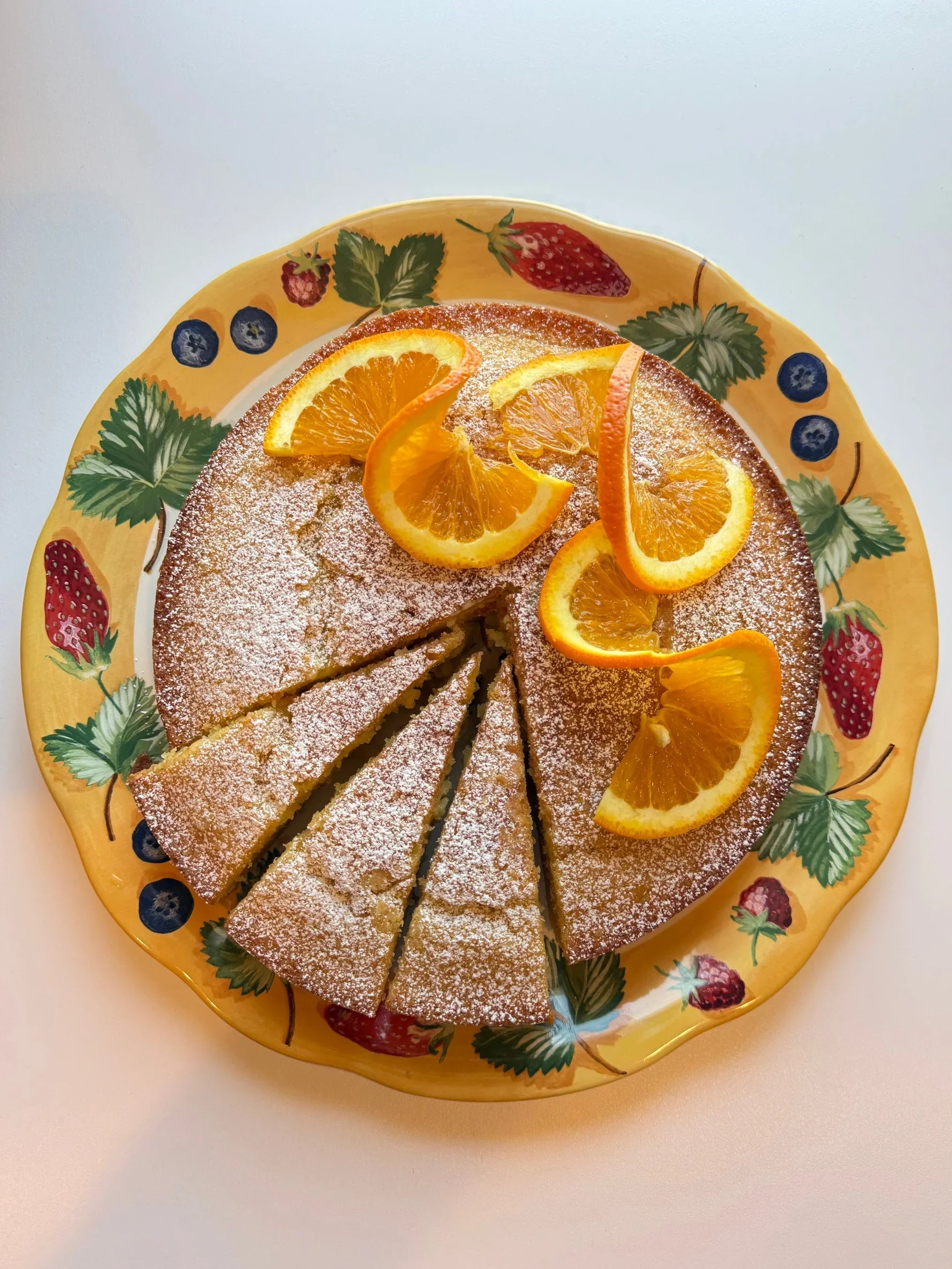 Beautiful orange olive oil cake dusted with powdered sugar and garnished with fresh orange slices and berries.